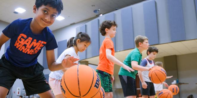 Group of sports camp participants practicing dribbling basketballs