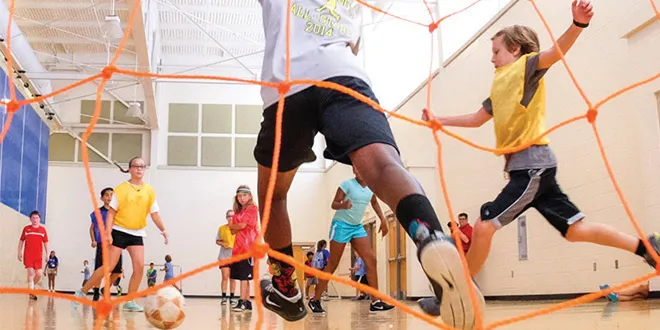 Kids and teens playing indoor soccer in a YMCA gym