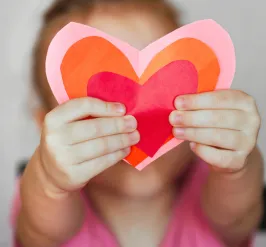 young girl holding up three colorful paper hearts