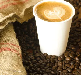 Coffee in a white plastic cup on a bed of espresso beans
