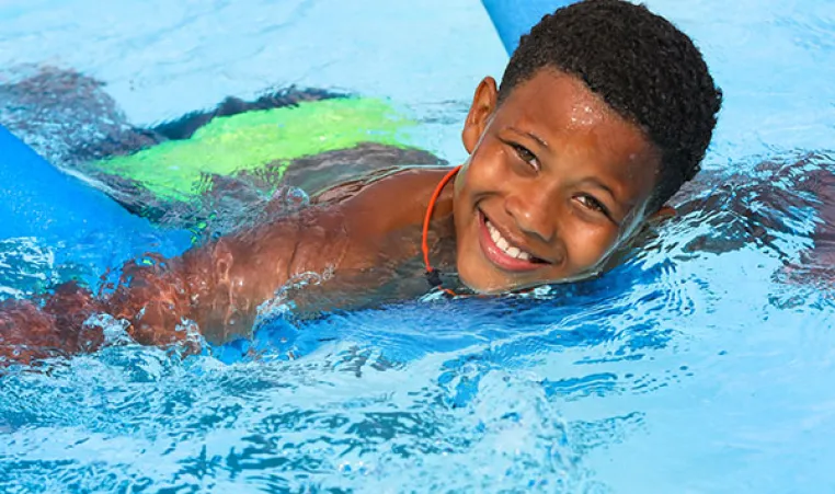 Young boy swimming with a pool noodle 