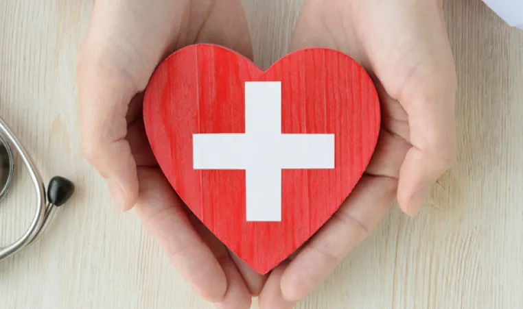 Doctor's hands holding a wooden heart with a first-aid cross.