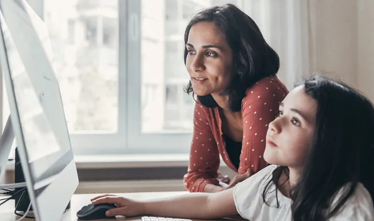 a girl and her mother work together on a Mac