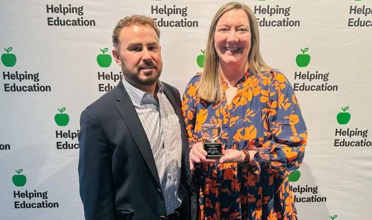 woman holds an award next to a man in front of a backdrop