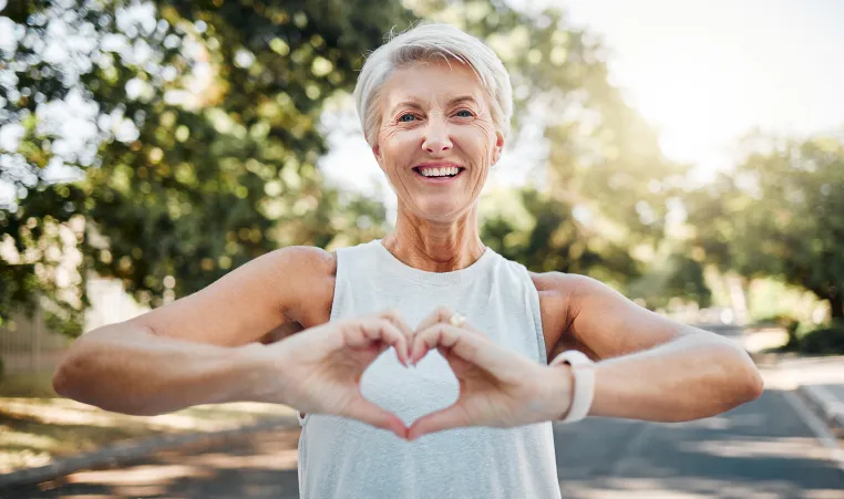 healthy older woman out for a run and making a heart with her hands