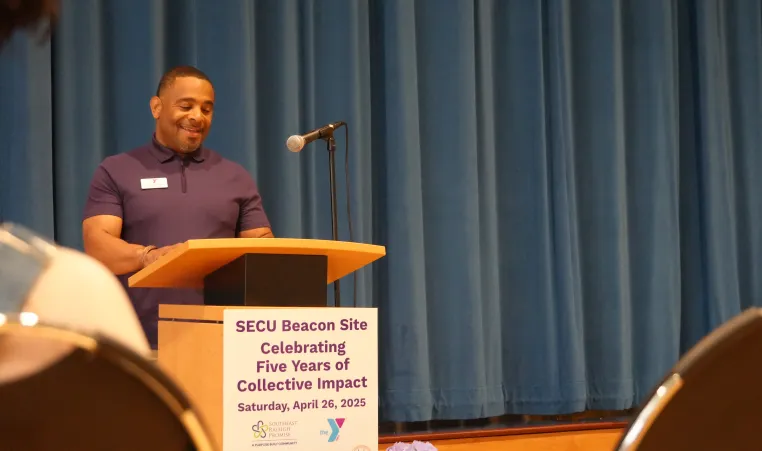 image of man at podium with sign that says SECU Beacon Site Celebrating Five Years of Collective Impact