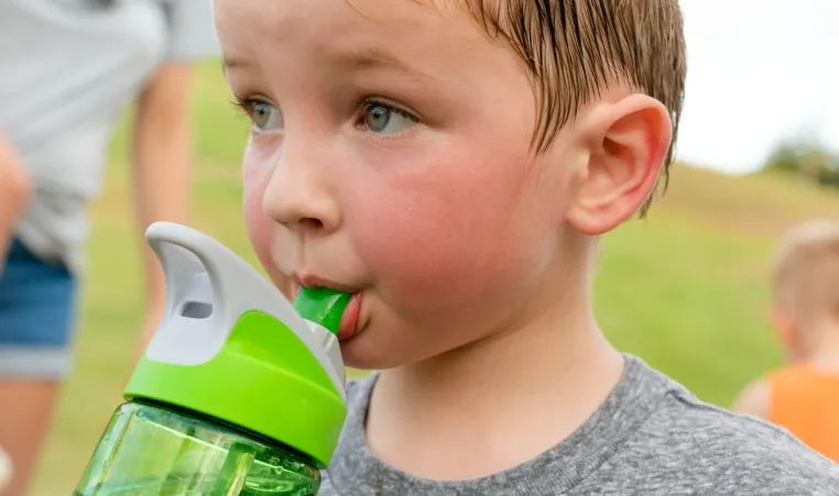 child drinks from water bottle on hot day