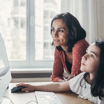 a girl and her mother work together on a Mac