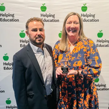 woman holds an award next to a man in front of a backdrop