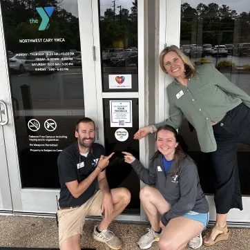 ymca staff members point to sticker recognizing the y as an IDD inclusive employer