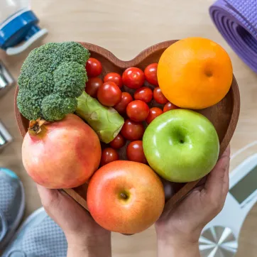 collection of fruits and vegetables in a heart-shaped bowl, held over pieces of fitness equipment
