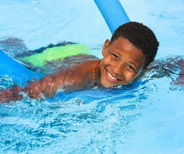 Young boy swimming with a pool noodle