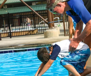 Young boy jumping into the pool with YMCA instructor