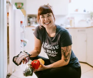 a woman holding healthy food in front of a refrigerator
